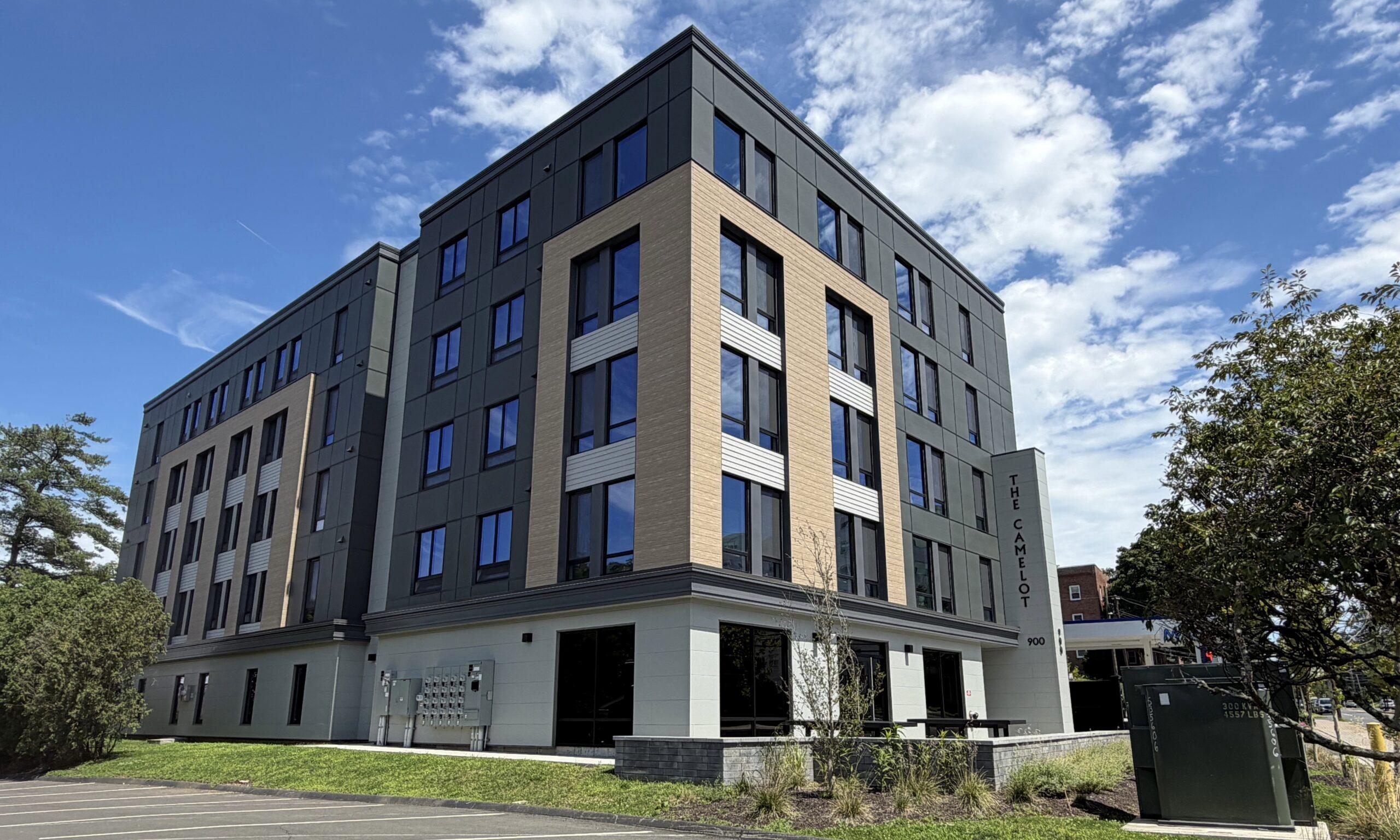 Exterior corner of a modern apartment building with a gray and wood-tone facade under a blue sky