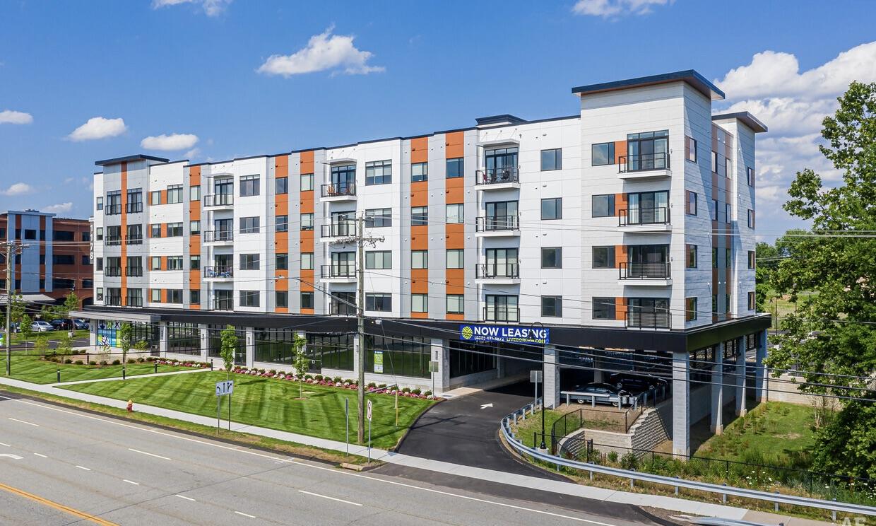 Exterior of a modern five-story apartment building with orange accent panels and ground-floor retail