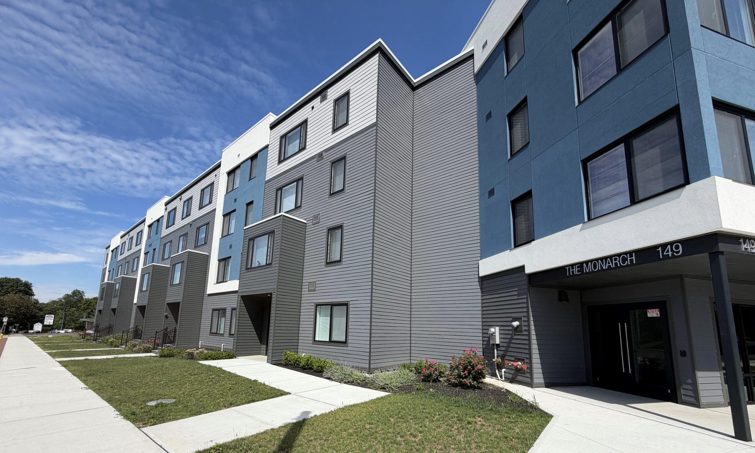 Side exterior of The Monarch apartment building, a modern gray structure beside a sidewalk
