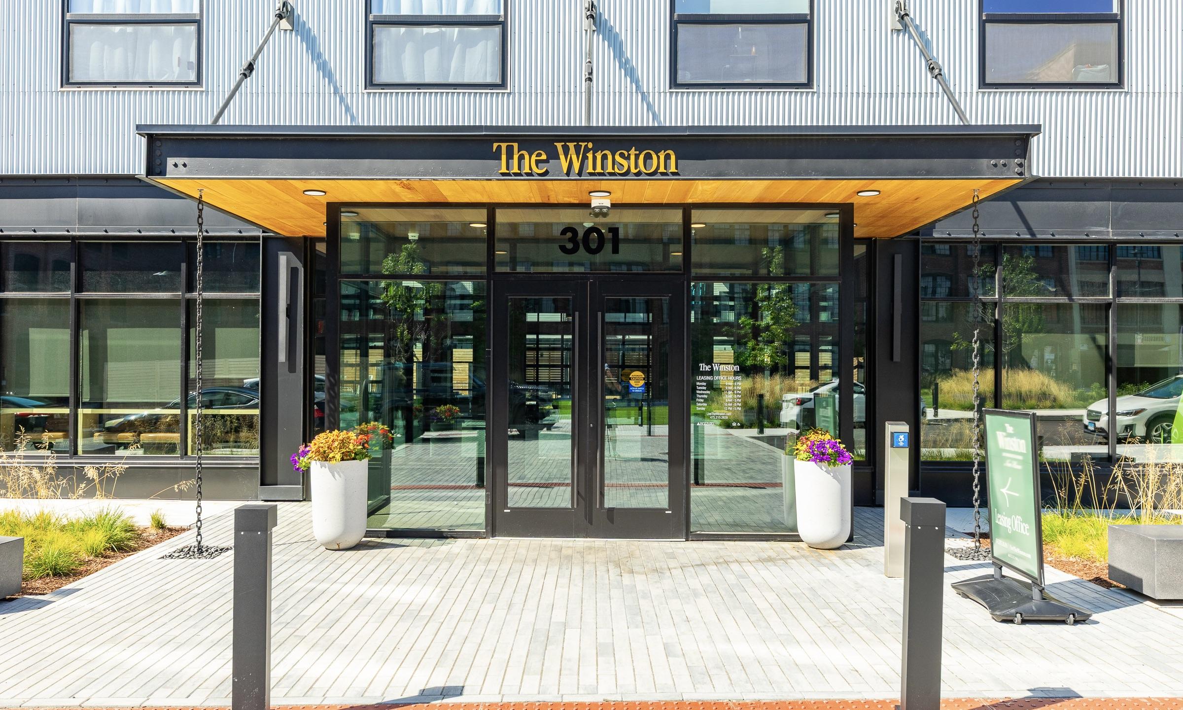 Glass entrance canopy of The Winston building with its address sign and planters