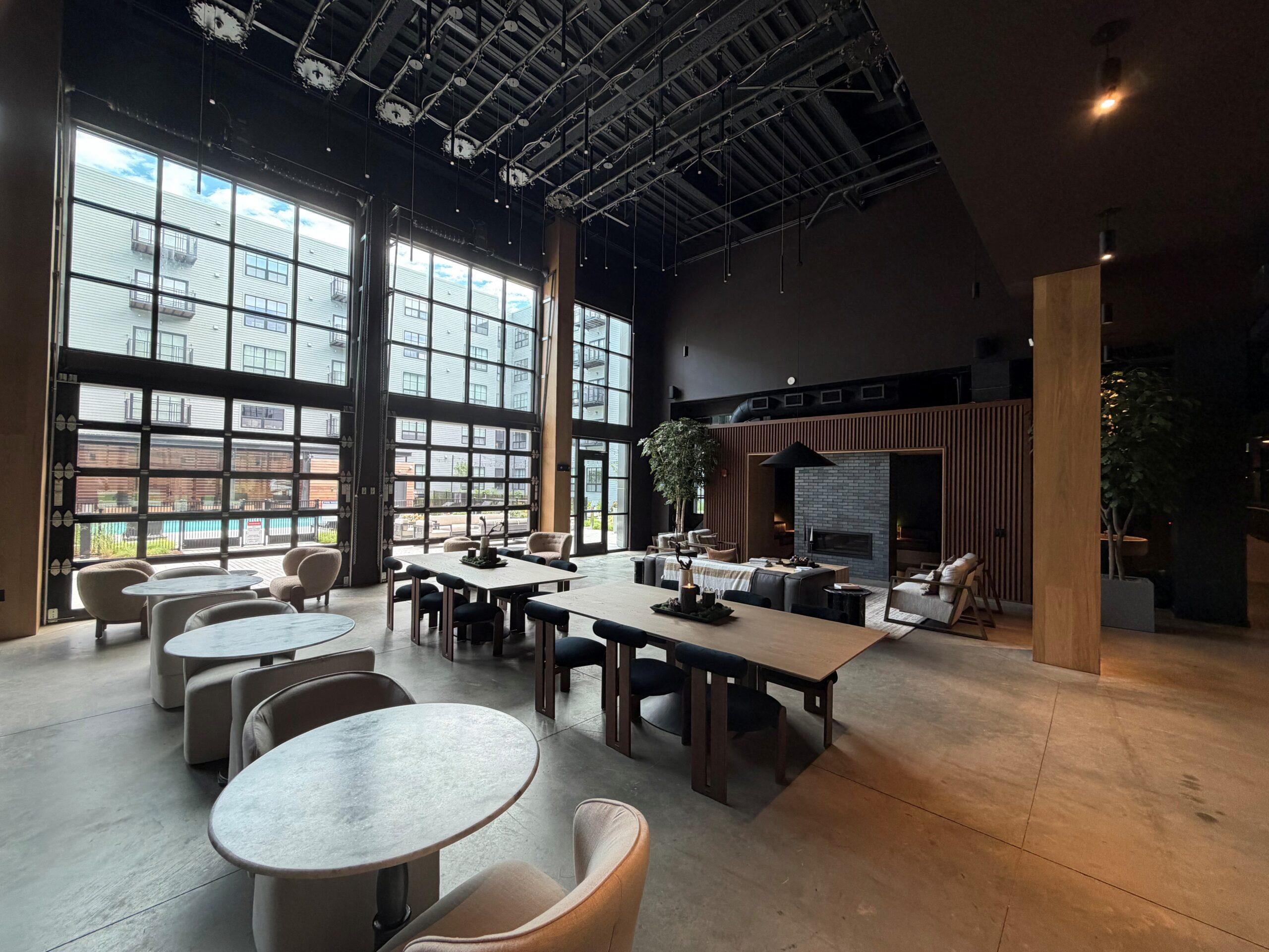 Community lounge at The Winston Apartment community lounge with floor-to-ceiling windows, a long communal table, and a dark exposed ceiling