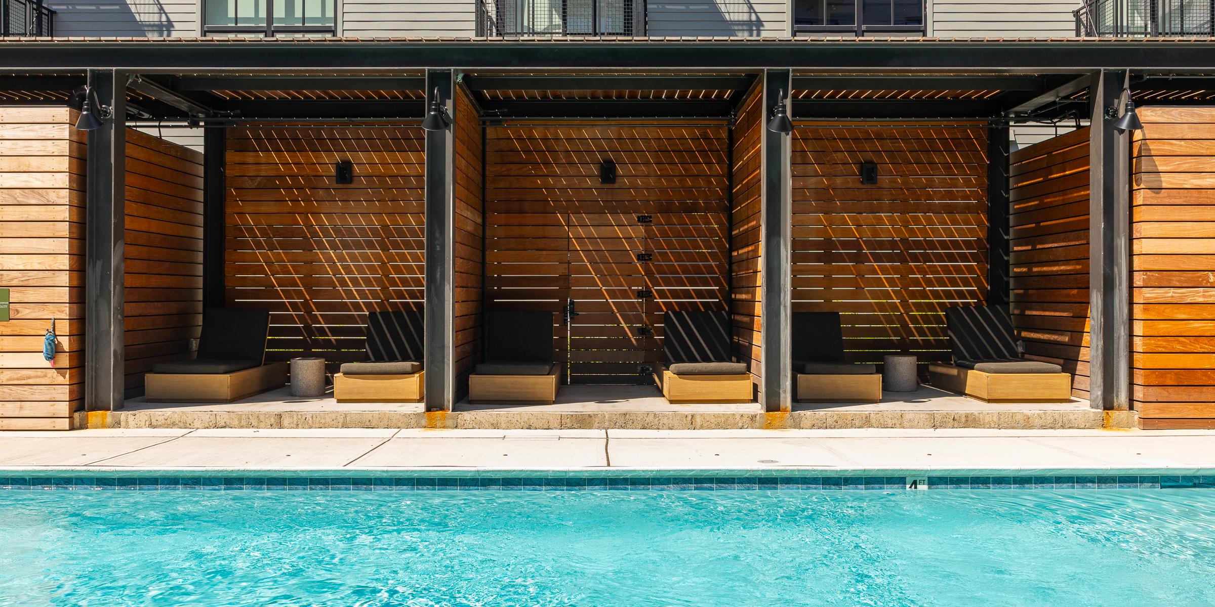 Cabanas at the pool at The Winston Resort-style pool with wood cabanas and lounge chairs at an apartment community