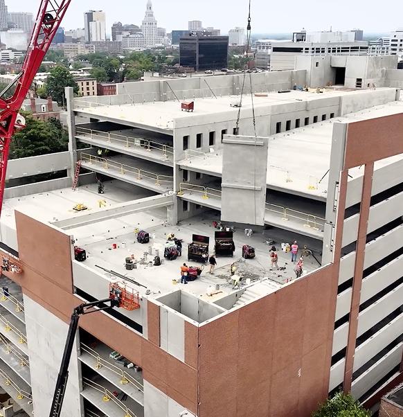 Aerial view of a multi-level concrete parking garage under construction with a red crane